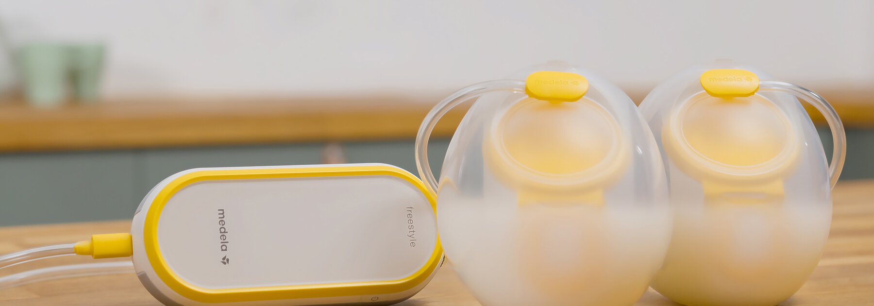 Freestyle™ Hands-free double electric wearable breast pump Medela Freestyle™ Handsfree dubbele elektrische draagbare borstkolf zittend op aanrecht met opvangbekers gevuld met melk