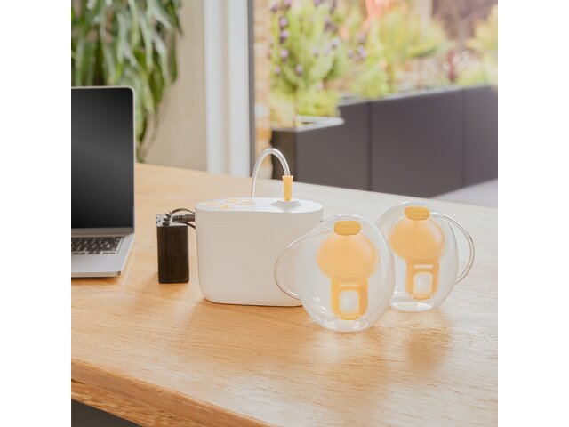 Medela Pump In Style® Hands-free double electric breast pump sitting on office desk with the pump, Hands-free collection cups and battery pack charger