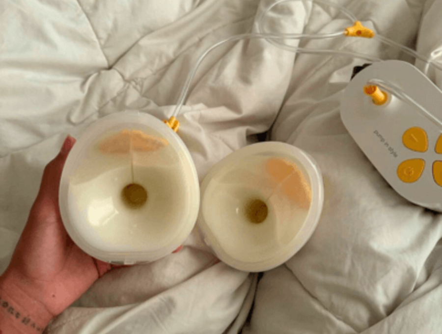 Pump In Style Hands-free breast pump with full collection cups sitting on white down comforter.