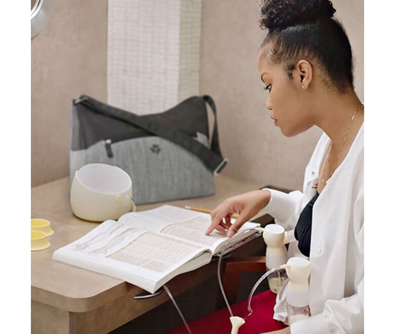 Mom reading a book while double pumping with her Medela Sonata® Smart double electric breast pump