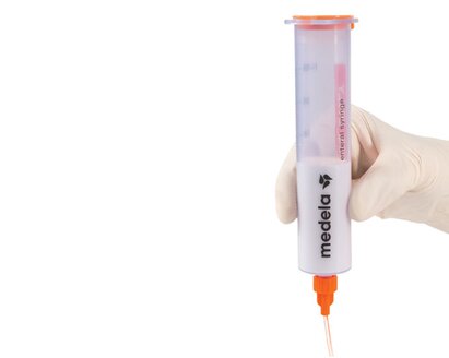 A Medela GraviFeed® Syringe with ENFit® Connector and tubing held by someone's hand wearing a surgical glove.