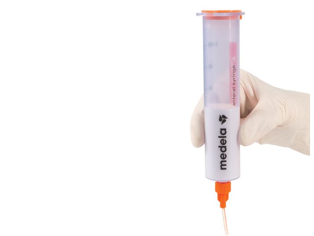 A Medela GraviFeed® Syringe with ENFit® Connector and tubing held by someone's hand wearing a surgical glove.