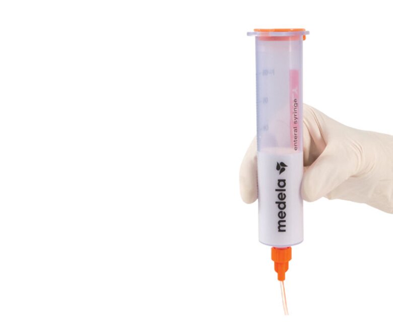 A Medela GraviFeed® Syringe with ENFit® Connector and tubing held by someone's hand wearing a surgical glove.