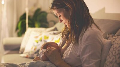 A mom breastfeeding her baby at night in her living room with the lights dimmed.