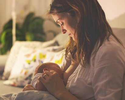 A mom breastfeeding her baby at night in her living room with the lights dimmed.