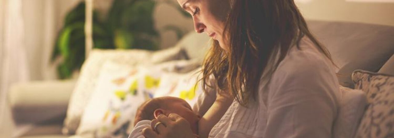 A mom breastfeeding her baby at night in her living room with the lights dimmed.