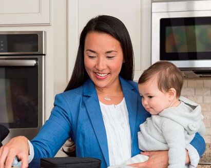 A mom getting ready to go to work while holding her baby on her hip in the kitchen.