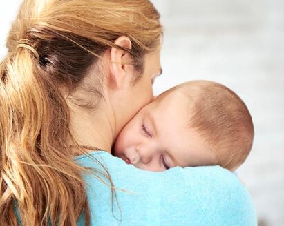 A mother holds her baby close to her body as it sleeps in her arms.