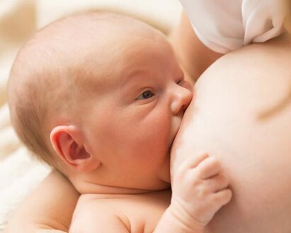 A newborn baby nursing on large breasts.