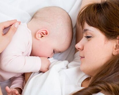 A mom watches as her baby sleeps in the bed next to her.