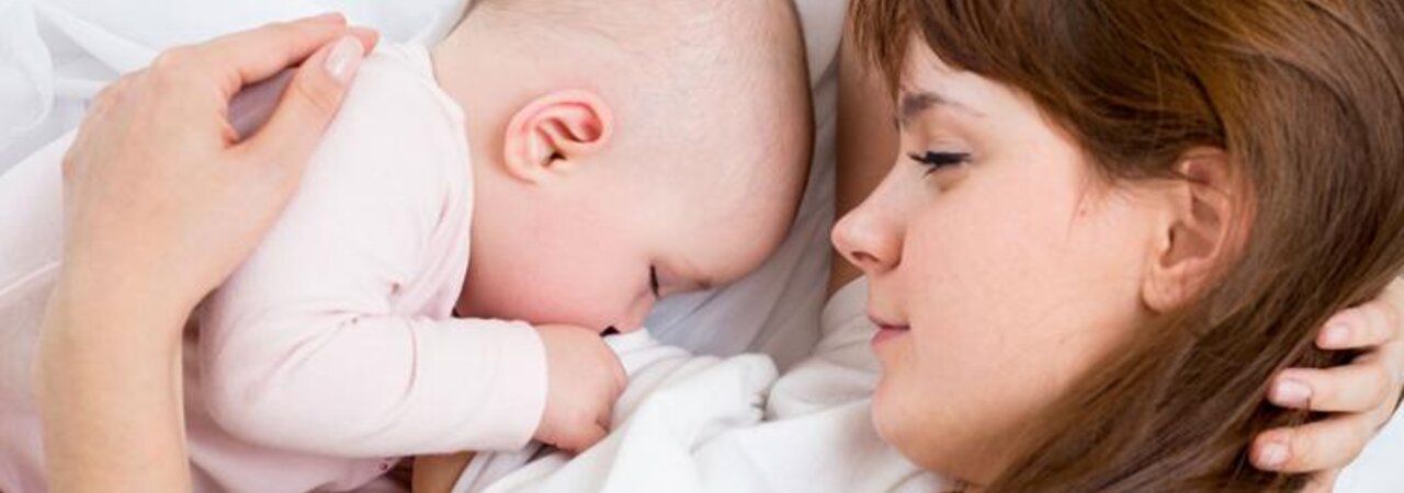 A mom watches as her baby sleeps in the bed next to her.