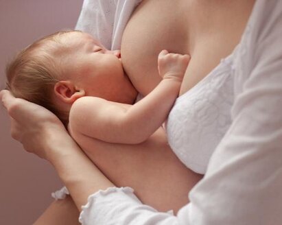 A mother supports the head of her newborn baby while it is being breastfed.