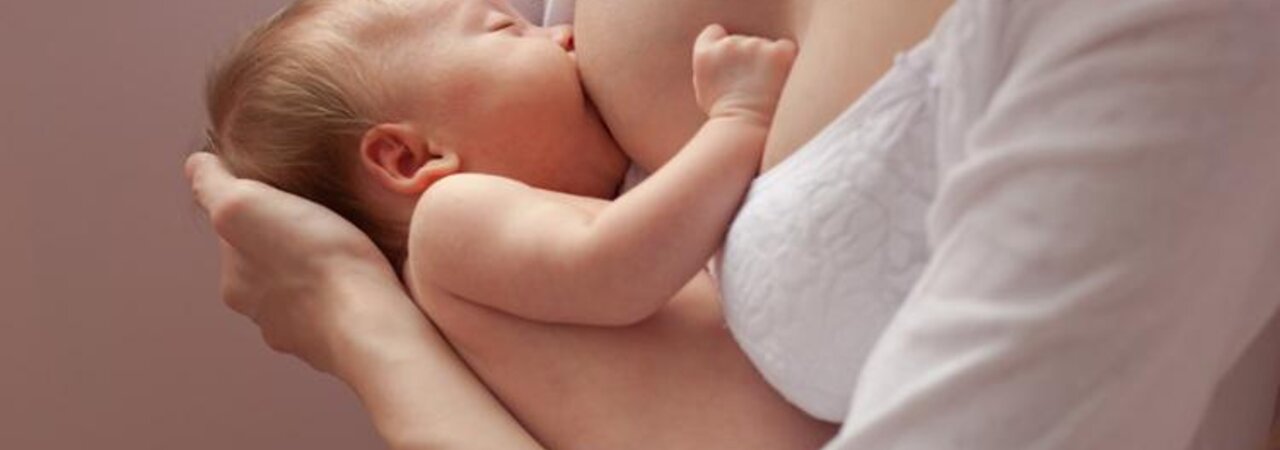 A mother supports the head of her newborn baby while it is being breastfed.