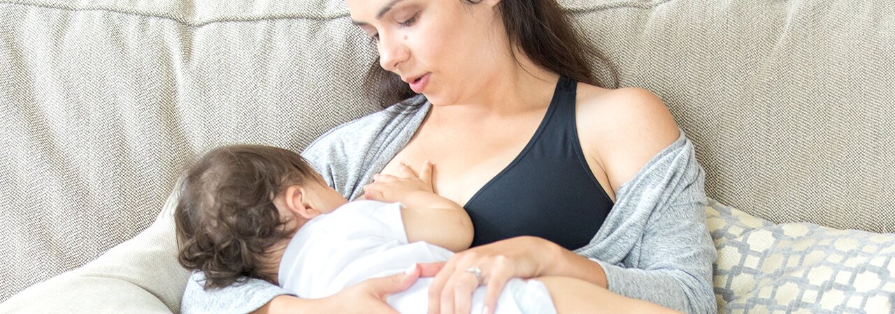 A mother breastfeeding her baby while wearing a Medela maternity bra.