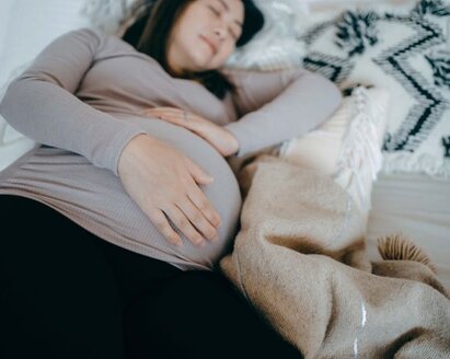 Una donna incinta giace addormentata su un fianco nel letto, tenendosi il pancione.