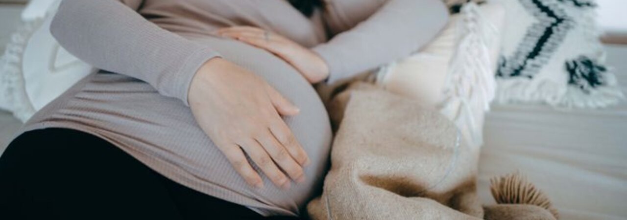 Una donna incinta giace addormentata su un fianco nel letto, tenendosi il pancione.