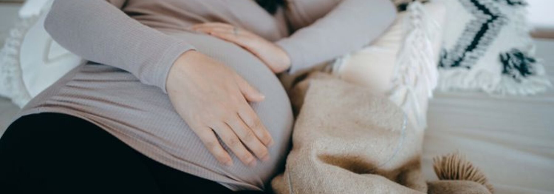 Een zwangere vrouw ligt op haar zij in bed te slapen en houdt haar zwangere buik vast.