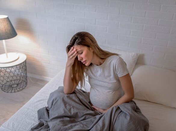 Zwangere moeder zit met ongemak in bed.