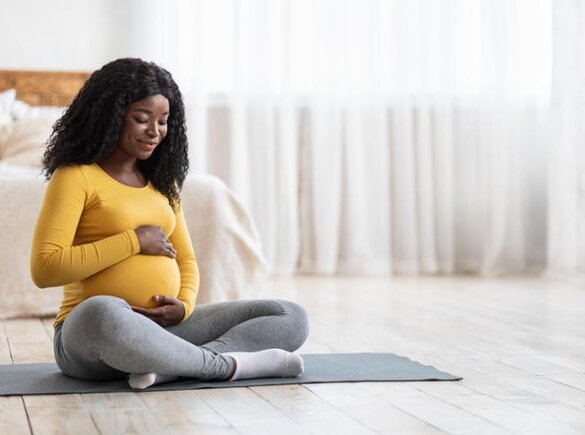 Zwangere moeder zittend op een yogamat.