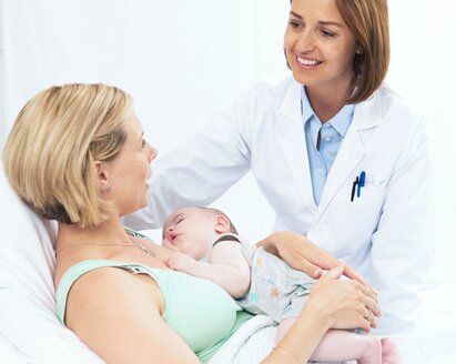 Un bébé dort sur la poitrine de sa mère pendant qu'elle parle à un professionnel de la santé.