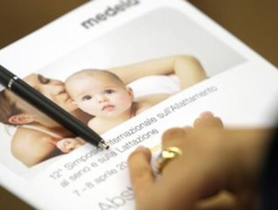 De hand van een vrouw rust op een Medela-boekje waaraan een pen is bevestigd.