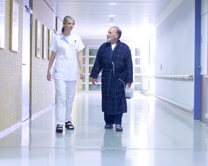 A doctor and a patient walk down a hospital corridor.