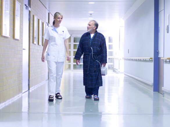 A doctor and a patient walk down a hospital corridor.