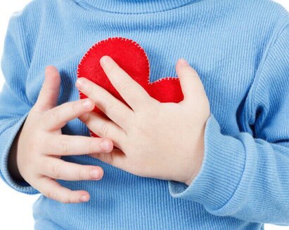 Ein Kind, das sich einer Kinderherzoperation unterziehen muss, hält ein Herz aus Stoff in der Hand.