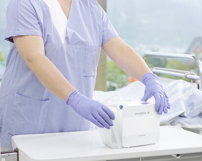 A healthcare professional works with the Medela Thopaz+ while a patient rests on a bed in the hospital.