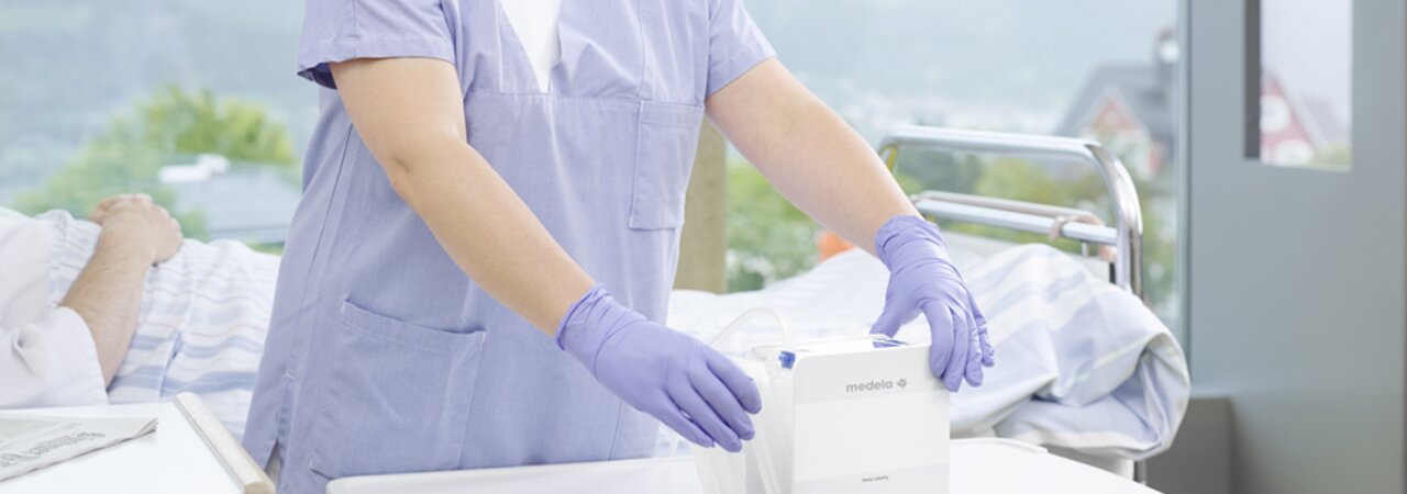 A healthcare professional works with the Medela Thopaz+ while a patient rests on a bed in the hospital.