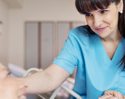 Medical professional leaning over bed rail of elderly patient.