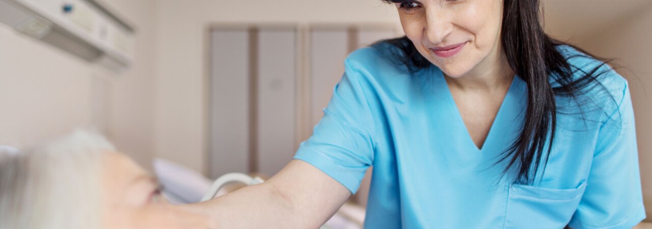 Medical professional leaning over bed rail of elderly patient.