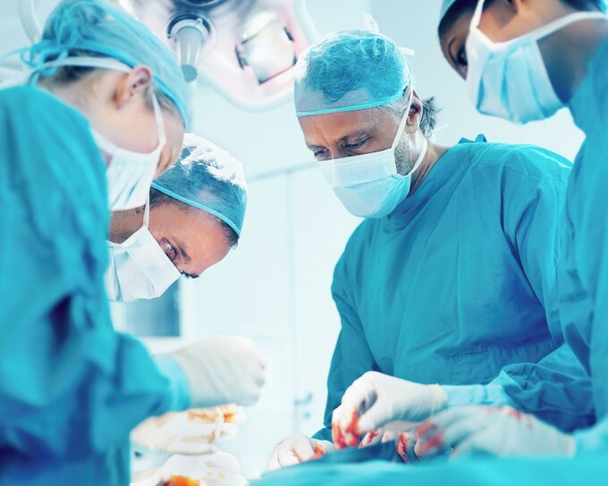 Operationssaal mit mehreren Ärzten, die auf einen Patienten herabblicken.