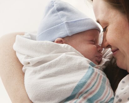 A mother holds her wrapped newborn baby close to her face in hospital.