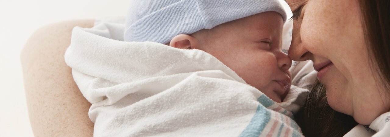 A mother holds her wrapped newborn baby close to her face in hospital.