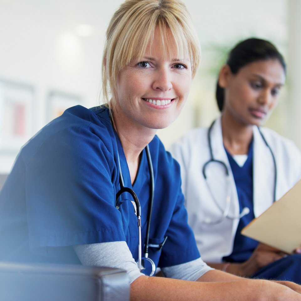 One doctor smiling at camera other doctor looking at a chart.