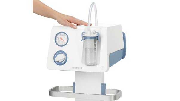 A hands rests on the top of a Medela Mobile Basic Surgical Suction Pump.