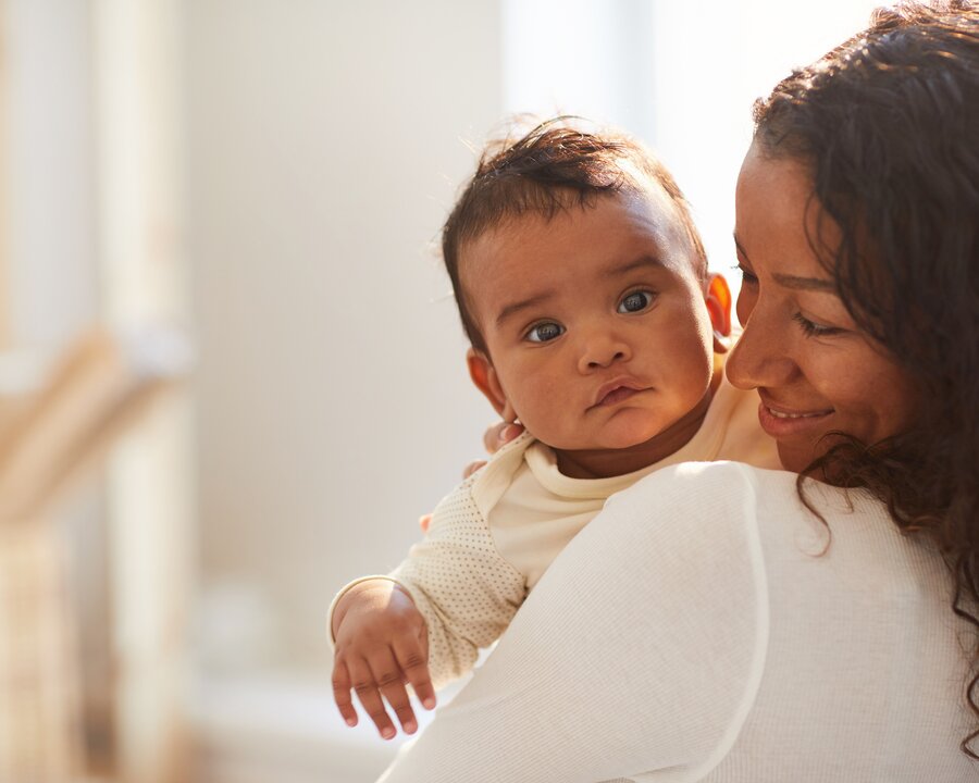 Een moeder houdt haar baby vast en kijkt ernaar terwijl de baby naar de camera kijkt, buiten.
