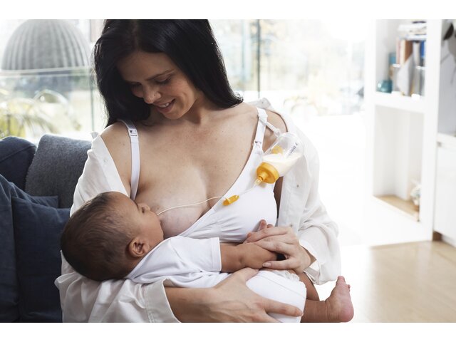 A mom breastfeeding her baby and supplementing the diet using Medela's Supplemental Nursing System™ (SNS).