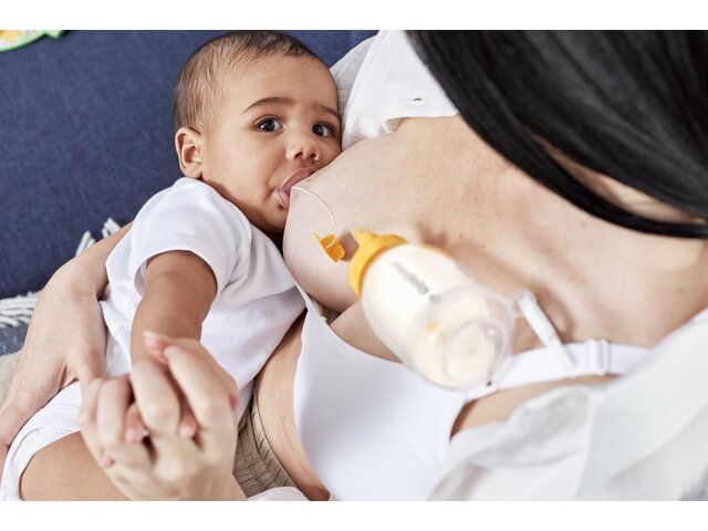 A mom breastfeeding her baby and supplementing the diet using Medela's Supplemental Nursing System™ (SNS).