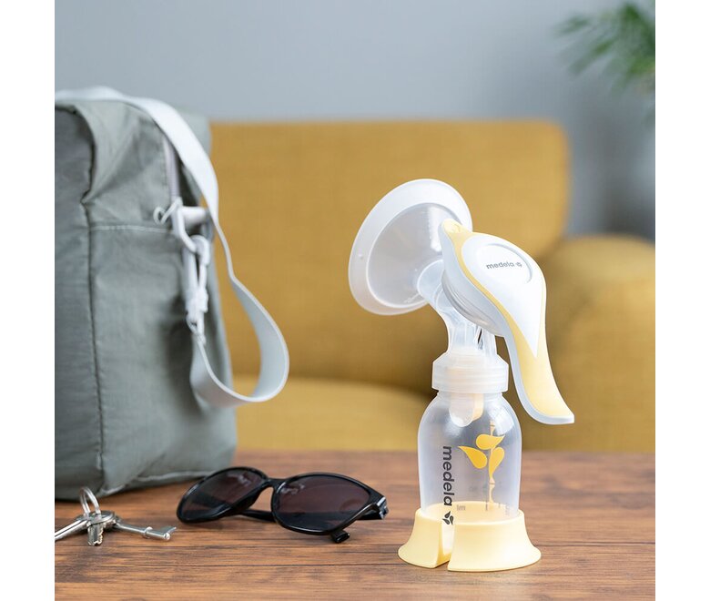 A bomba tira leite manual Medela Harmony™ em cima de uma mesa em casa, pronta a levar as chaves, os óculos e o saco das fraldas.