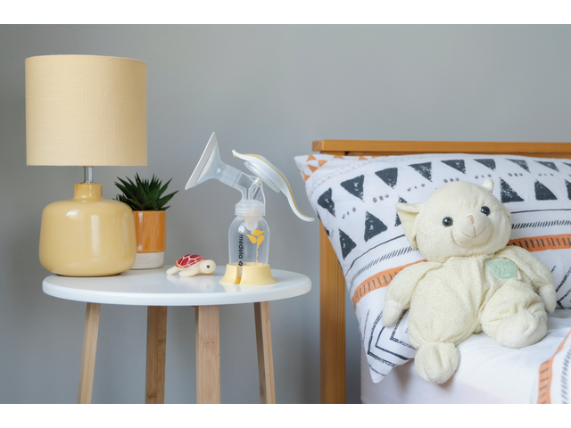 Medela Harmony breast pump sitting on table next to bed in a nursery.