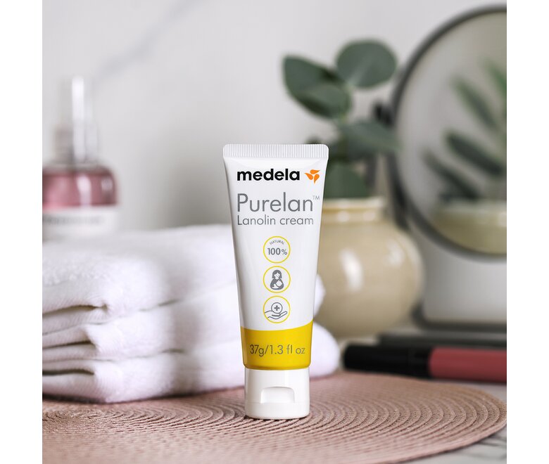 Medela Purelan™ lanolinecrème op het aanrecht naast een plant en handdoeken.