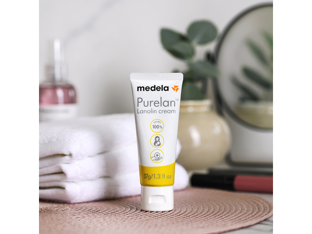 Medela Purelan™ lanolin cream on a bathroom counter next to a plant and towels.