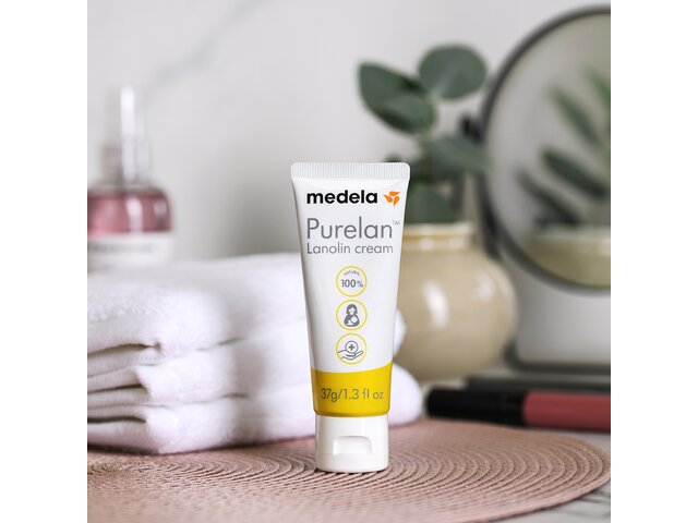 Medela Purelan™ Lanolincreme auf einem Badezimmertisch neben einer Pflanze und Handtüchern.