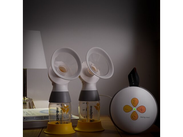 The Medela Swing Maxi™ double electric breast pump with two Classic collection containers on a bedside table with dimmed light.