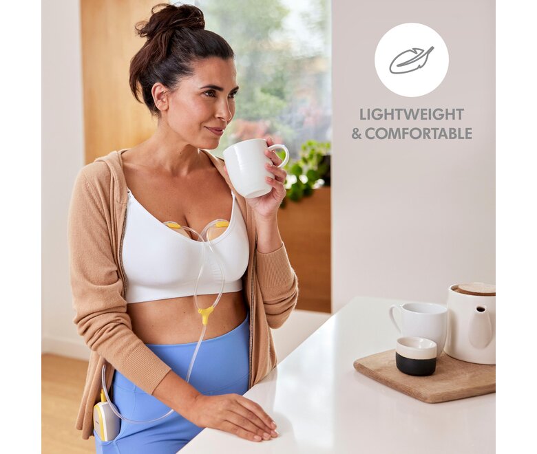 Mãe a beber café enquanto usa a sua bomba tira leite Medela Freestyle™ Hands-free, dupla e eléctrica. O texto da imagem diz: “Leve e confortável”.
