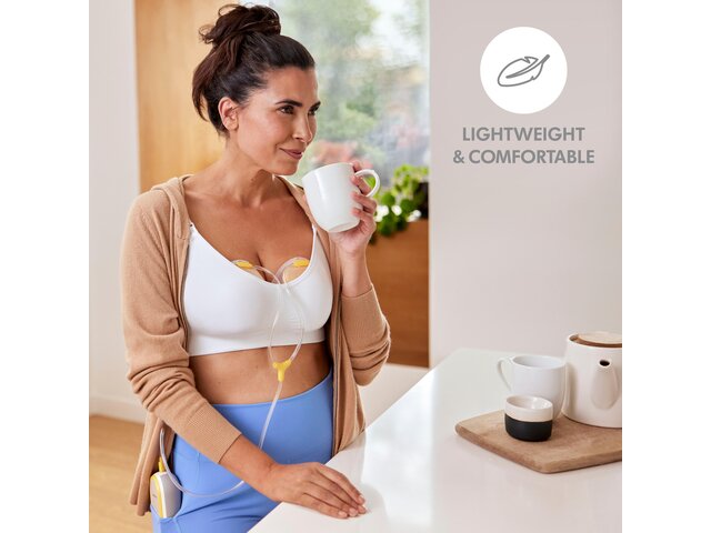 Mom drinking coffee while wearing her Medela Freestyle™ Hands-free double electric wearable breast pump. Image text says, "Lightweight and comfortable."