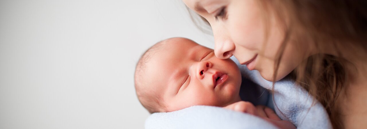 A mother holds her sleeping newborn close to her face.