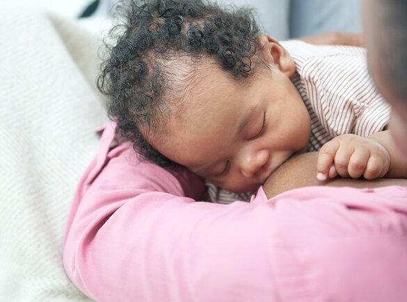 Un bambino che allatta in grembo alla mamma mentre è a casa.